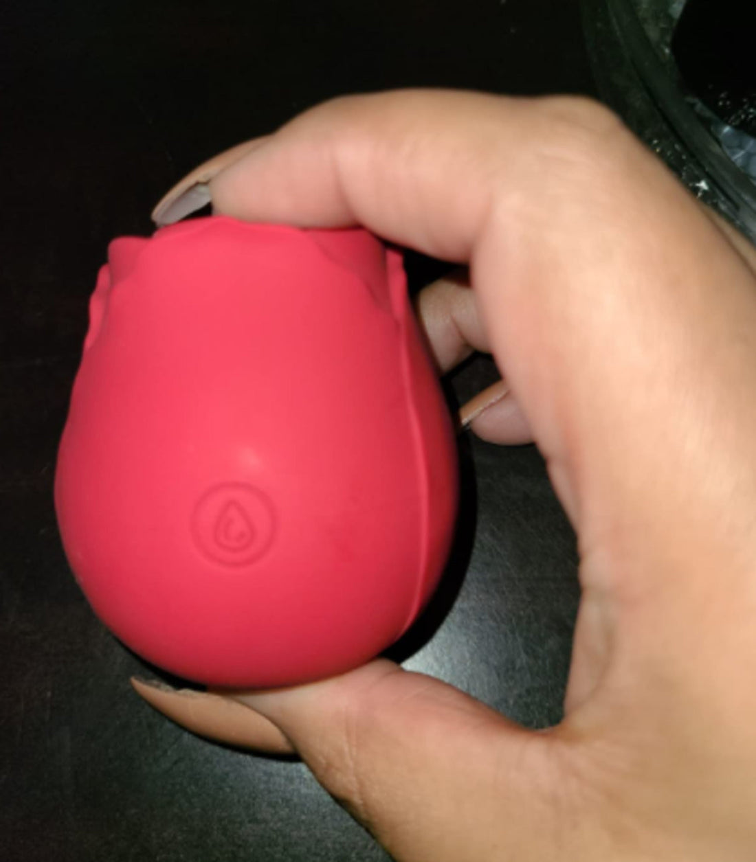 Pink rose toy held between the fingers of one hand, showing the power button