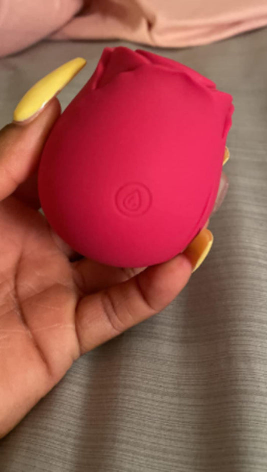 Pink rose toy held in a hand with the power button facing the camera