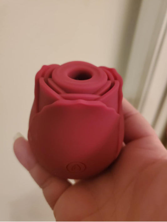 Dark red rose toy held in a hand, showing the petal design and the suction opening
