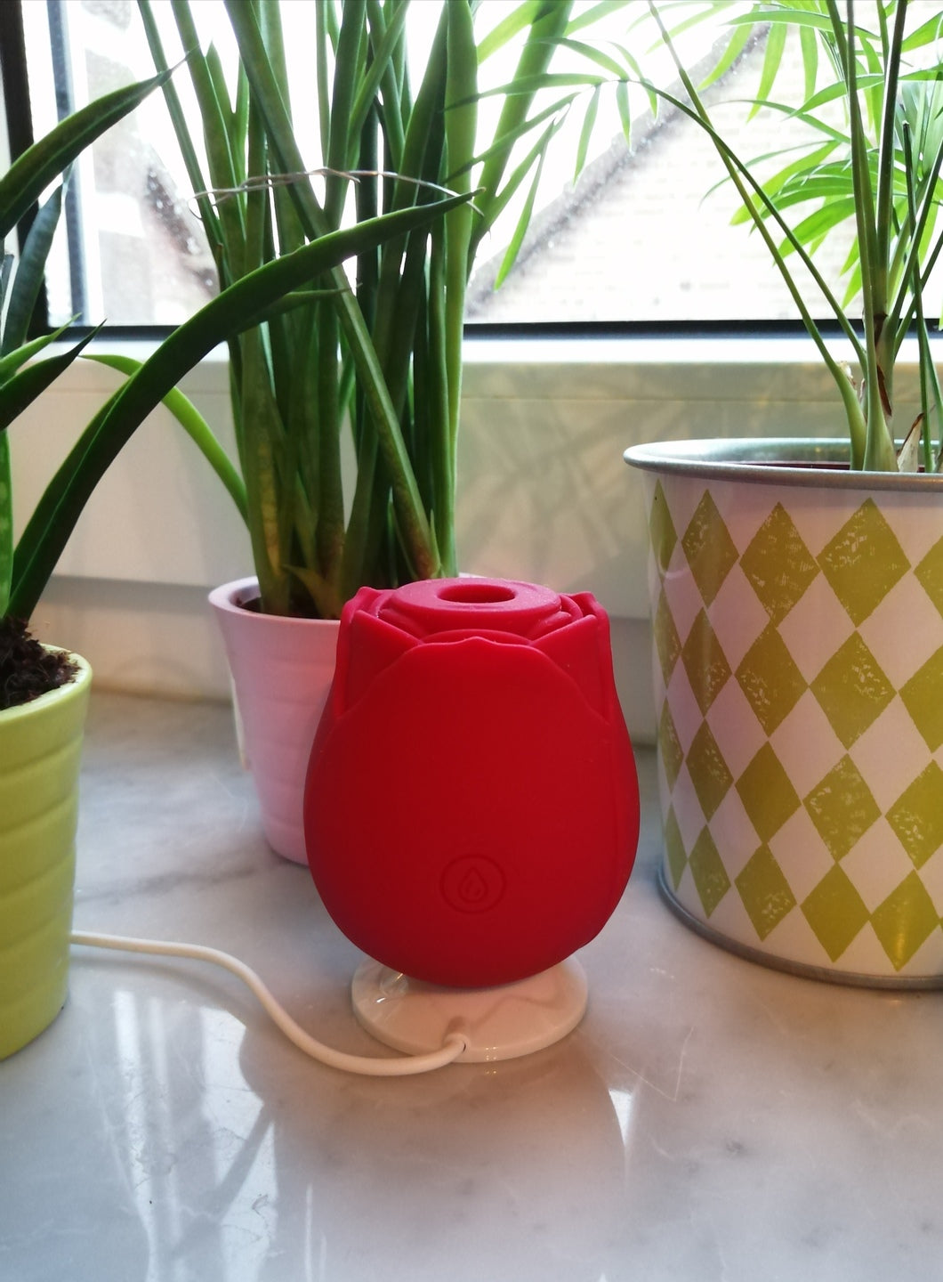 Rose toy charging on its magnetic dock, red rose toy vibrator on a windowsill