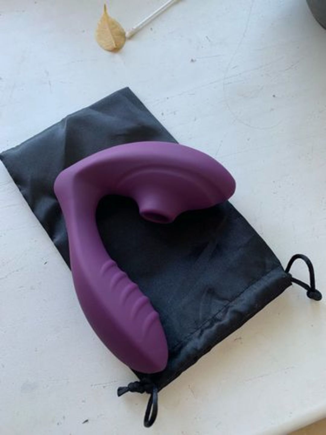 Purple suction vibrator resting on a black drawstring storage pouch on a white surface.