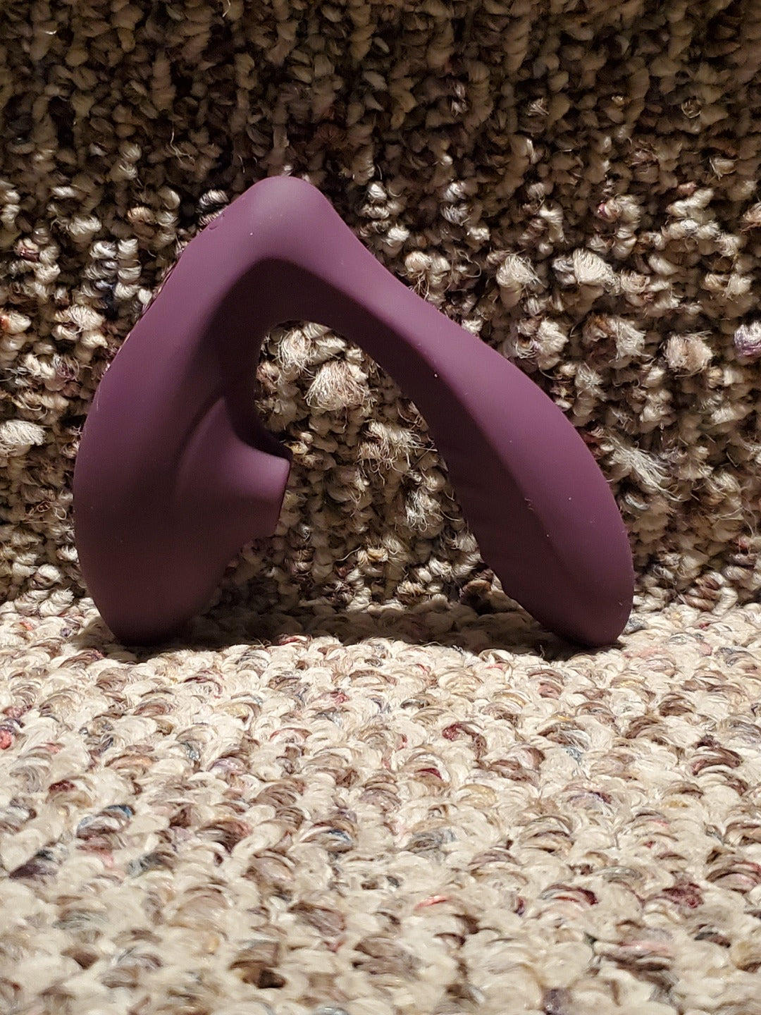Purple suction vibrator standing upright on a carpet, seen from the side with its C-shaped body.